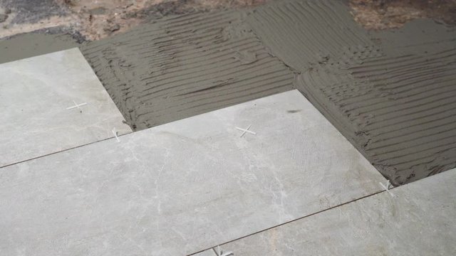 A close look at the construction tiler worker laying down the tile on cemented floor. Professional worker laying tiles on floor at construction site close-up slow motion.
