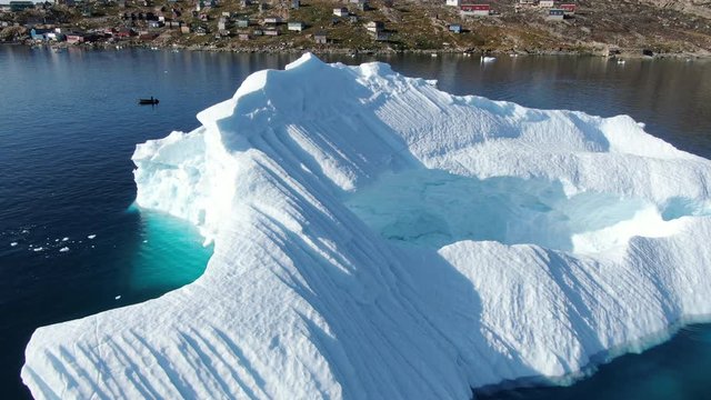 Ascending drone view of the island of Kullorsuaq, Greenland, showing a highly detailed scenery with icebergs floating in the deep blue arctic sea, little houses build on the rocky terrain