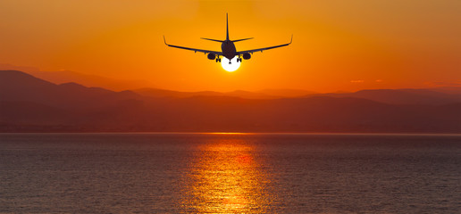 Airplane flying to the sunset over the sea-