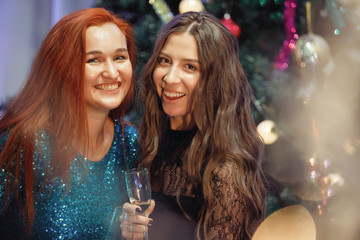 Beautiful women with a glass of champagne near a Christmas tree.
