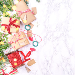 Craft boxes and wraps packed as Christmas gifts and red ribbons on white marble background with festive bokeh lights. Holiday season concept. Square, place for text
