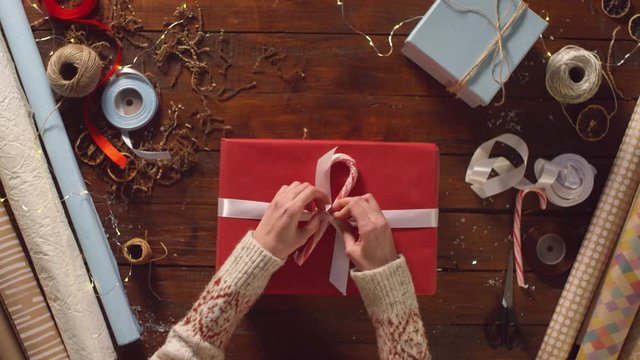 Top view of hands of woman untying ribbon with candy cane, opening red gift box and taking plush bear toy while unpacking Christmas present on wooden table