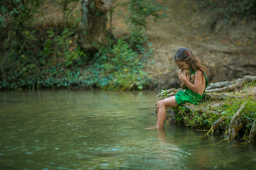 Girl 5-6 years old a small child sitting on the Bank of the river with his feet in the river.