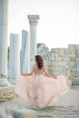 Adult woman between antique columns of architecture dressed in a long stylish light dress.