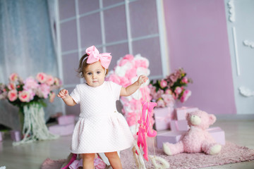 Baby with a pink dress on a background of pink adornment with a pink bow on her head.