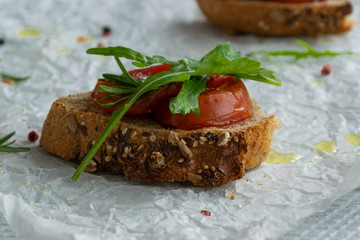 Delicious homemade bruschetta with whole grain bread, grilled tomatoes and fresh arugula. Vegetarian healthy snack, vegan food