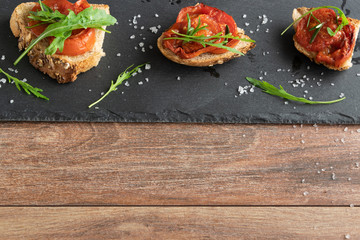 Delicious homemade bruschetta with whole grain bread, grilled tomatoes and fresh arugula. Vegetarian healthy snack, vegan food