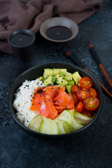 A popular Hawaiian dish, Poke in a plate of red fish, rice and vegetables. Poke plate on a black concrete background