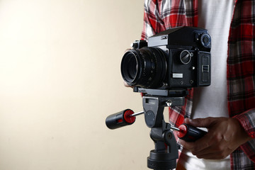 Adult man holding an old and vintage medium format film camera on a tripod.