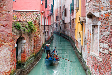 Obraz na płótnie Canvas Venetian gondolier punting gondola through green canal waters of Venice Italy