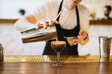 Pouring espresso martini from a shaker into a cocktail glass. Selective focus. Horizontal lifestyle image.