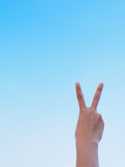 Human hand show victory sign gesture on sky background.