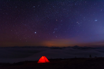 Fairytale landscapes of the winter Carpathian Mountains with a charming milky way in the sky tourist tents and snowy houses in the valleys	