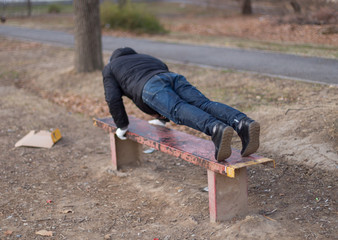 A young man does push ups on an iron park bench as he warms up for his daily workout or jogging