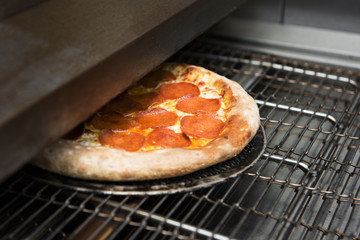 Preparing pizza in oven at restaurant kitchen, ready pizza from electric conveyor oven