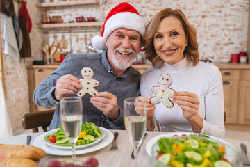 Positive delighted mature couple holding funny cookies