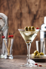 Classic Martini vodka cocktail, with dry vermouth, vodka and green olives, bar tools, vintage wood bar counter, selective focus