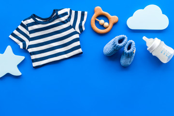 Newborn baby boy set - blue clothes as bodysuit, booties, toys - on blue table top-down frame copy space