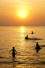 Naklejka na ściany i meble Silhouette children playing over yellow sunset beach
