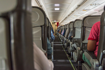 Walking aisle and passengers in economy class cabin on airplane