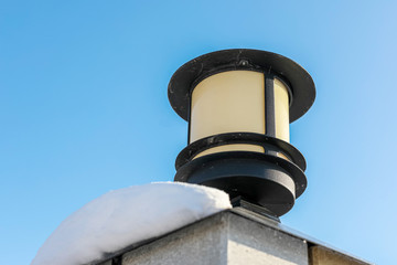 Modern street lamp is  on iron fence in winter.