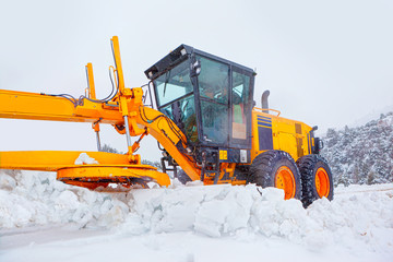 Bulldozer cleans snow-covered road through the forest.