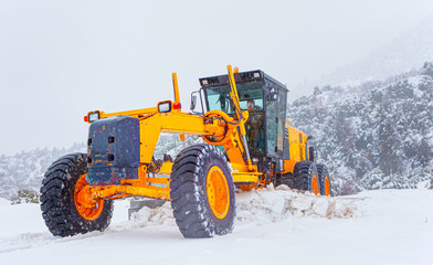 Bulldozer cleans snow-covered road through the forest.