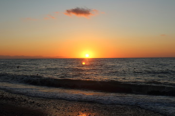the sun setting behind the promontory with the sea in the foreground