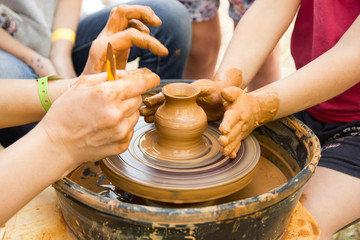 A close up view on ceramic production process on potter's wheel with children. Clay crafts with kids concept.