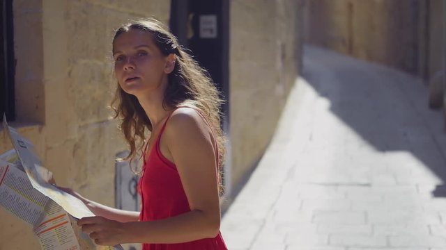 A young woman tourist is standing in the old city, with a map in his hands and looking for his whereabouts. Tourist with a map.