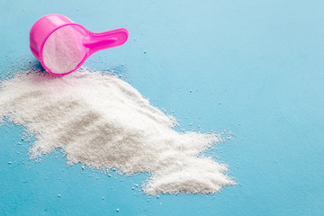 Household chemicals. Washing powder in plastic spoon on blue background