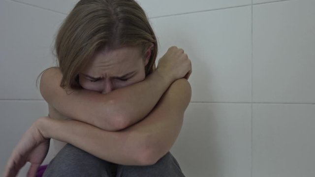 Woman with mental problem sufering for depression. Unhappy girl sitting at home bathroom with sad face expression.