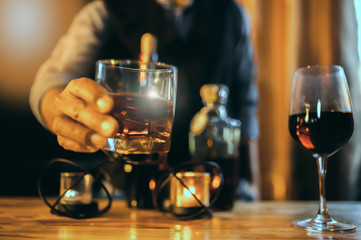 Hands of a bartender, with a glass of whiskey, soft focus.