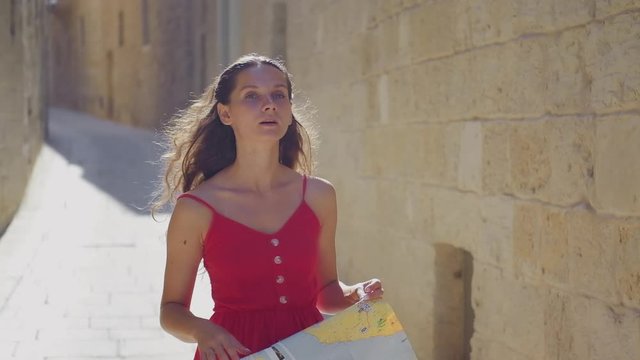A young woman tourist is standing in the old city, with a map in his hands and looking for his whereabouts. Tourist with a map.