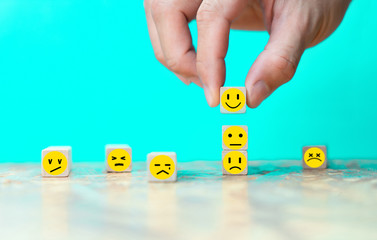 Businessman chooses a happy emoticon icons face on wooden block.