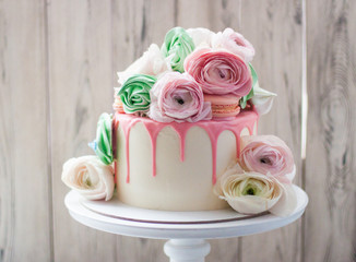 White cake with pink melted chocolate decorated with fresh flowers, roses, ranunculuses, macaroons...