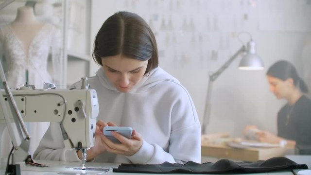 Woman seamstress looks at the smartphone screen in the workplace. Write text messages to customers