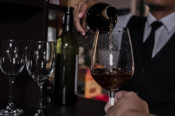 Waiter pouring wine into glasses at the bar.