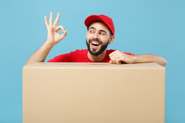 Delivery man in red uniform isolated on blue background, studio portrait. Male employee in cap...