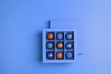 Handmade chocolates in a blue box on a neon blue background. Flat top view. Copy space. Holiday Concept Minimalism