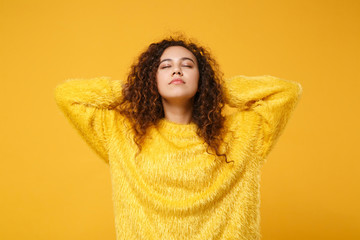 Relaxed young african american girl in fur sweater posing isolated on yellow orange wall background, studio portrait. People lifestyle concept. Mock up copy space. Sleeping with hands behind head.