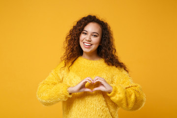 Smiling young african american girl in fur sweater posing isolated on yellow orange wall...