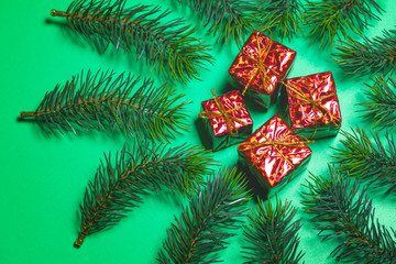 Top view of Christmas gift box red balls with spruce branches and bell on green background.