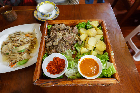 LHASA, TIBET / CHINA - July 29, 2017: Traditional tibetan food on a wooden plate - served in a restaurant near Barkhor Street / Jokhang temple. On the plate: yak meat, potatos, salad, sauce and spice.