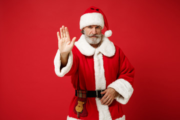Fototapeta na wymiar Elderly gray-haired mustache bearded Santa man in Christmas hat posing isolated on red background. Happy New Year 2020 celebration holiday concept. Mock up copy space. Showing stop gesture with palm.