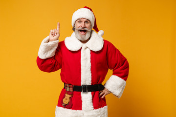 Fototapeta na wymiar Elderly gray-haired mustache bearded Santa man in Christmas hat posing isolated on yellow background. New Year 2020 celebration holiday concept. Mock up copy space. Hold finger up with great new idea.