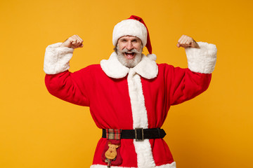 Fototapeta na wymiar Joyful elderly gray-haired mustache bearded Santa man in Christmas hat posing isolated on yellow wall background. Happy New Year 2020 celebration concept. Mock up copy space. Showing biceps, muscles.