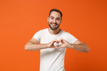 Smiling young man in casual white t-shirt posing isolated on orange wall background, studio...