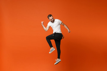 Fototapeta na wymiar Cheerful young man in casual white t-shirt posing isolated on bright orange wall background studio portrait. People lifestyle concept. Mock up copy space. Having fun, jumping, doing winner gesture.