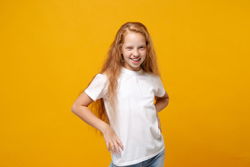 Charming little ginger kid girl 12-13 years old in white t-shirt isolated on yellow background children portrait. Childhood lifestyle concept. Mock up copy space. Standing with arms akimbo on waist.